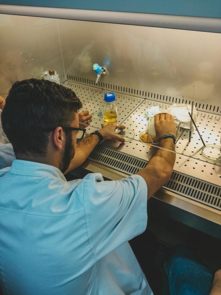 A male scientist in a lab coat works with petri dishes and equipment in a sterile environment.