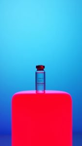 COVID-19 vaccine vial on a vibrant neon pink background against a blue gradient backdrop, symbolizing modern healthcare.