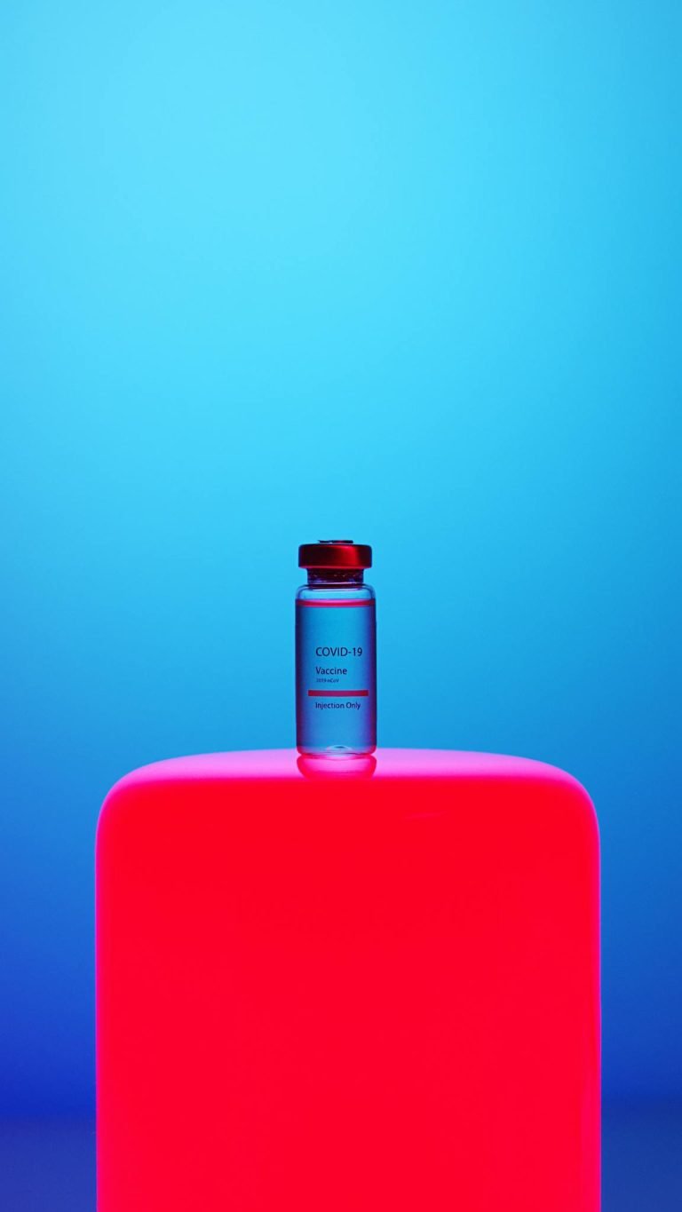 COVID-19 vaccine vial on a vibrant neon pink background against a blue gradient backdrop, symbolizing modern healthcare.